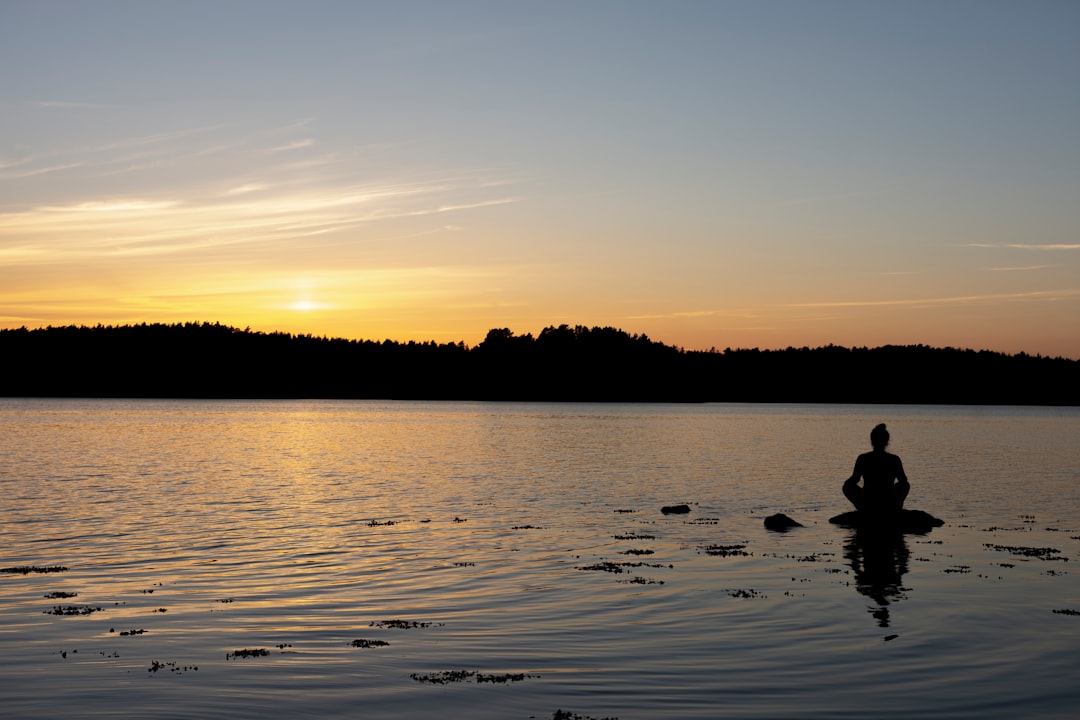 Person meditating in lotus position on yoga mat at sunset