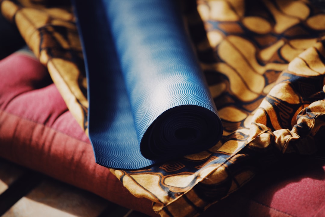 A rolled blue yoga mat resting on patterned fabric