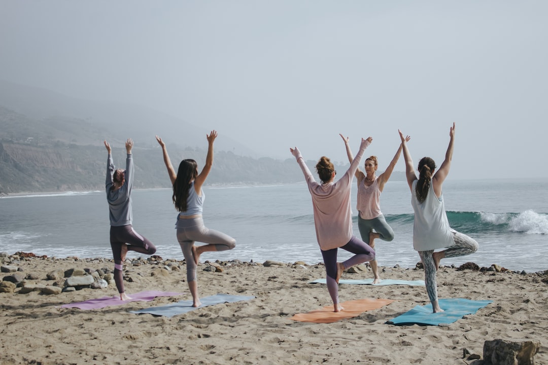 Group practicing tree pose balance on a beach at sunrise