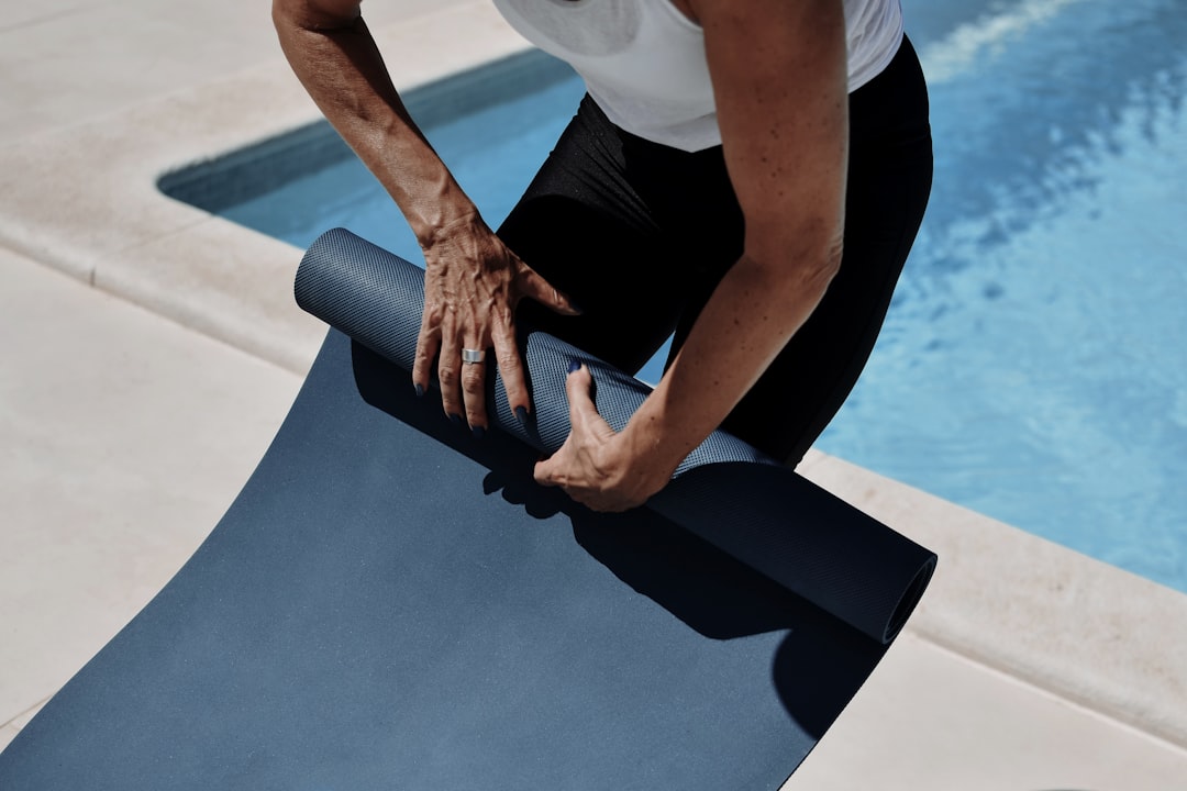 Person unrolling a blue yoga mat beside a pool