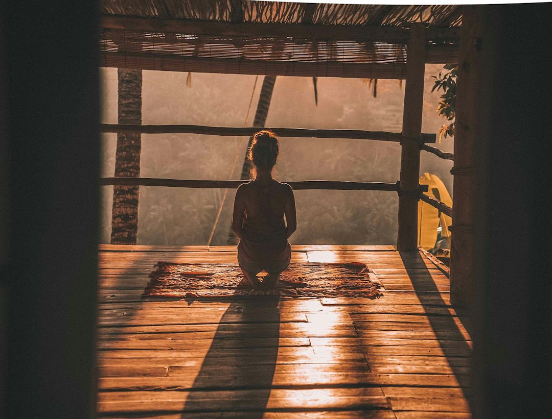 Woman kneeling in meditation on a mat in a sunlit wooden space