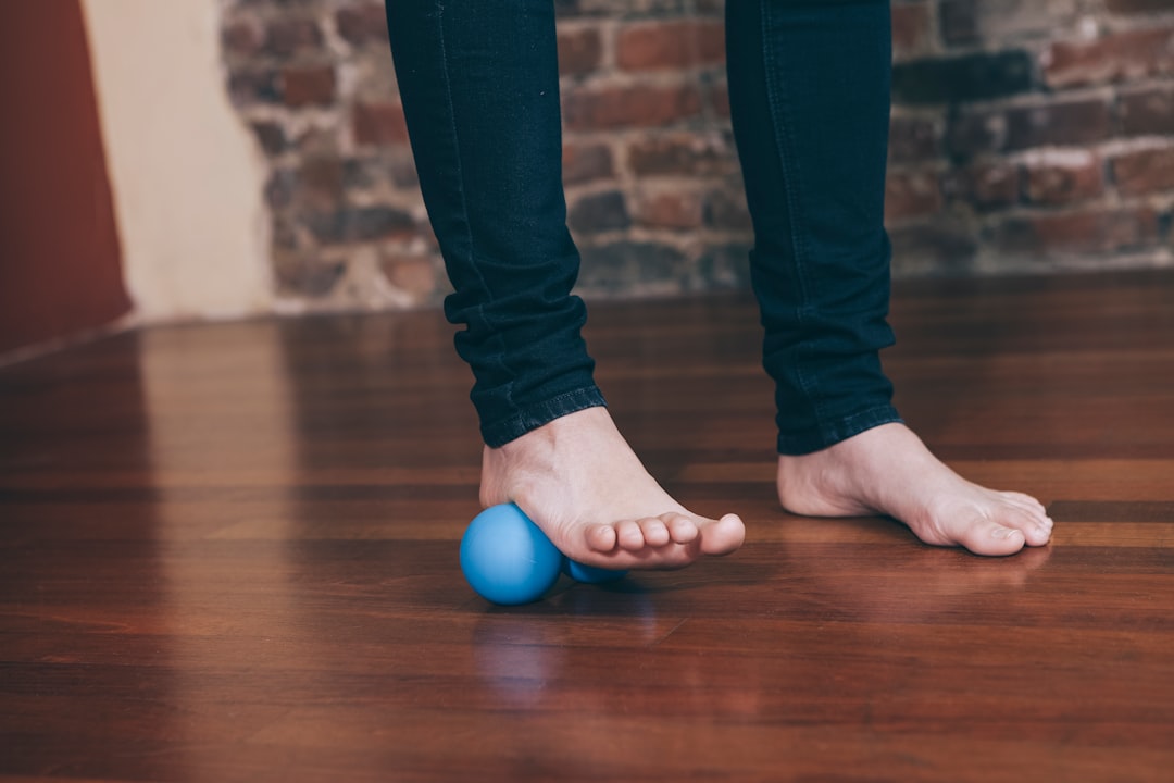 Person rolling a massage ball under a bare foot on a wooden floor