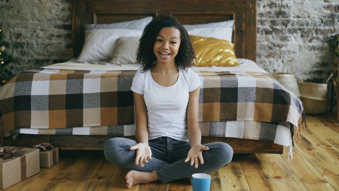 Smiling young woman sitting cross-legged on a bedroom floor, gesturing with her hands