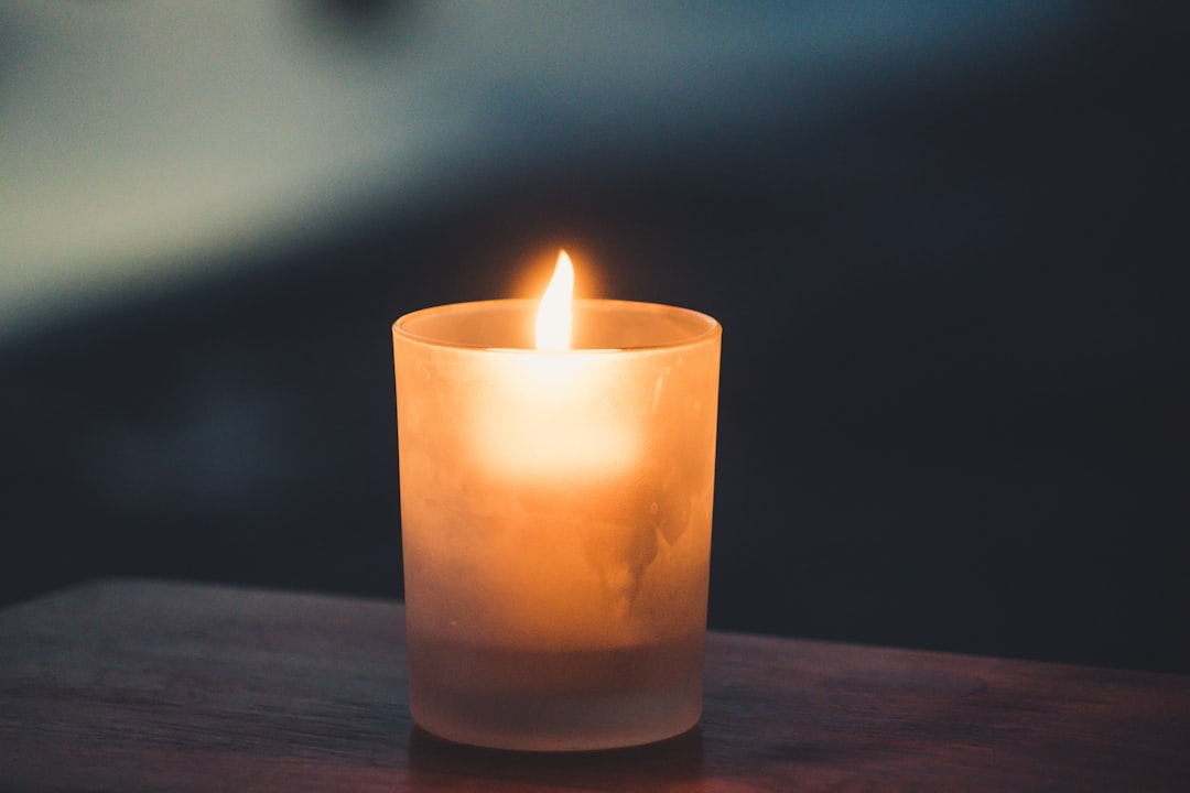 Single lit candle glowing in frosted glass on dark wood