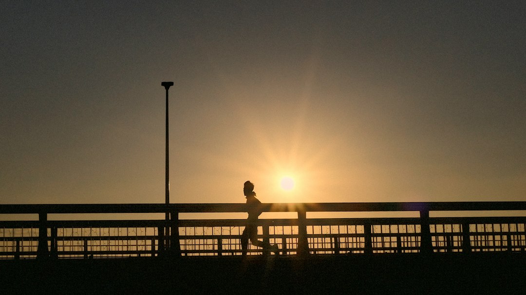 Silhouette of a runner crossing a bridge at sunset
