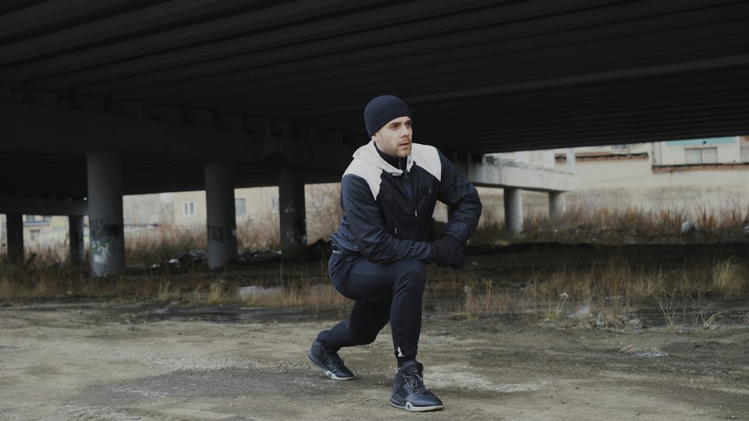 Man in athletic wear stretching his legs in a deep lunge under an overpass