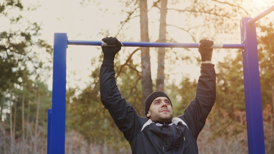 A man dead-hanging from an outdoor pull-up bar to build supporting grip strength