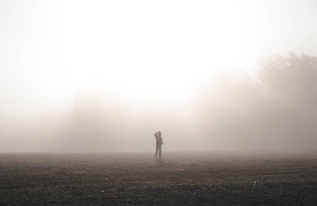 Person standing in thick fog on an open field at dawn