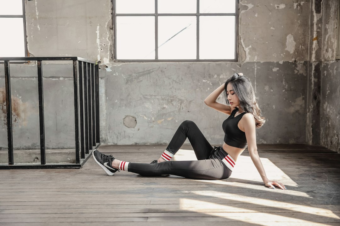 Fit woman in black athletic wear seated on a wooden floor in a loft space