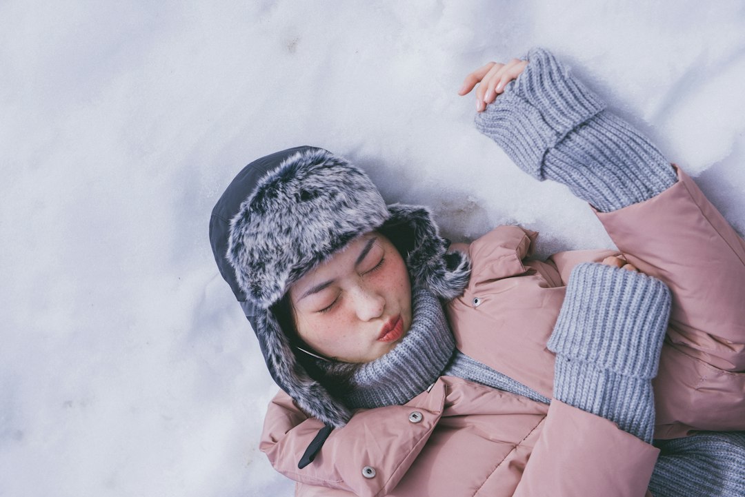 Woman in a winter coat lying relaxed in the snow with eyes closed