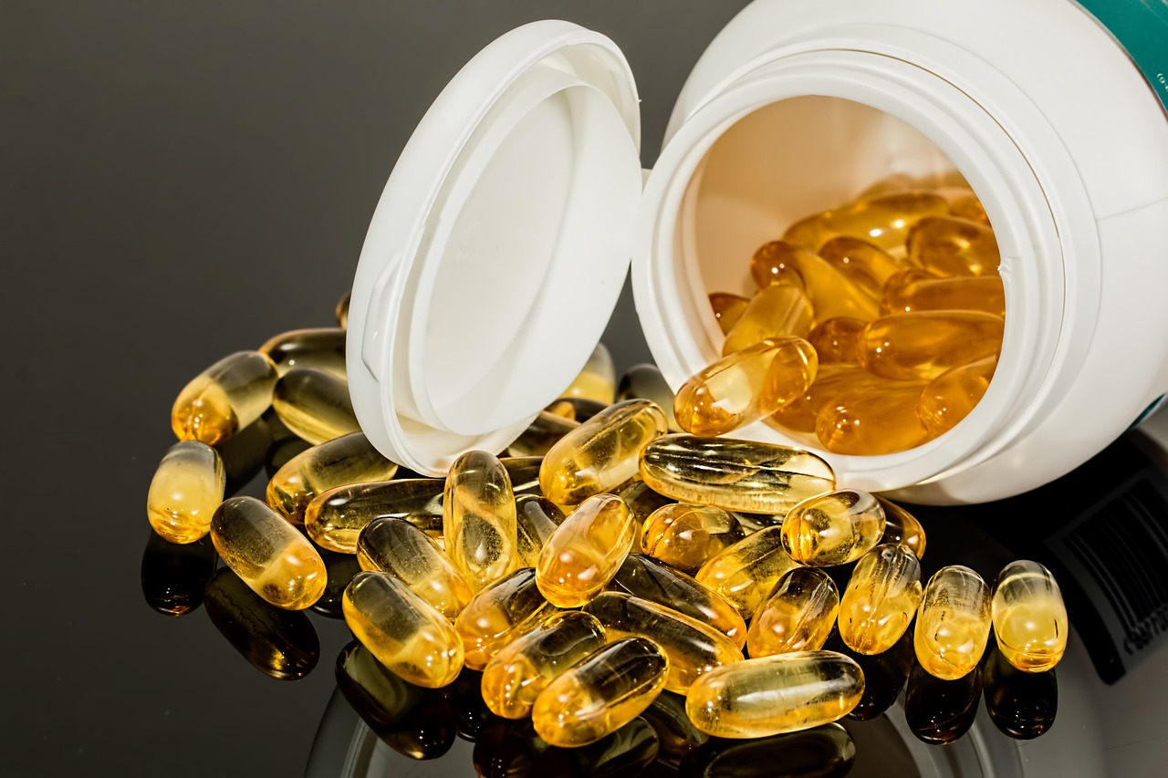 Clear softgel capsules spilling from a white supplement bottle onto a table