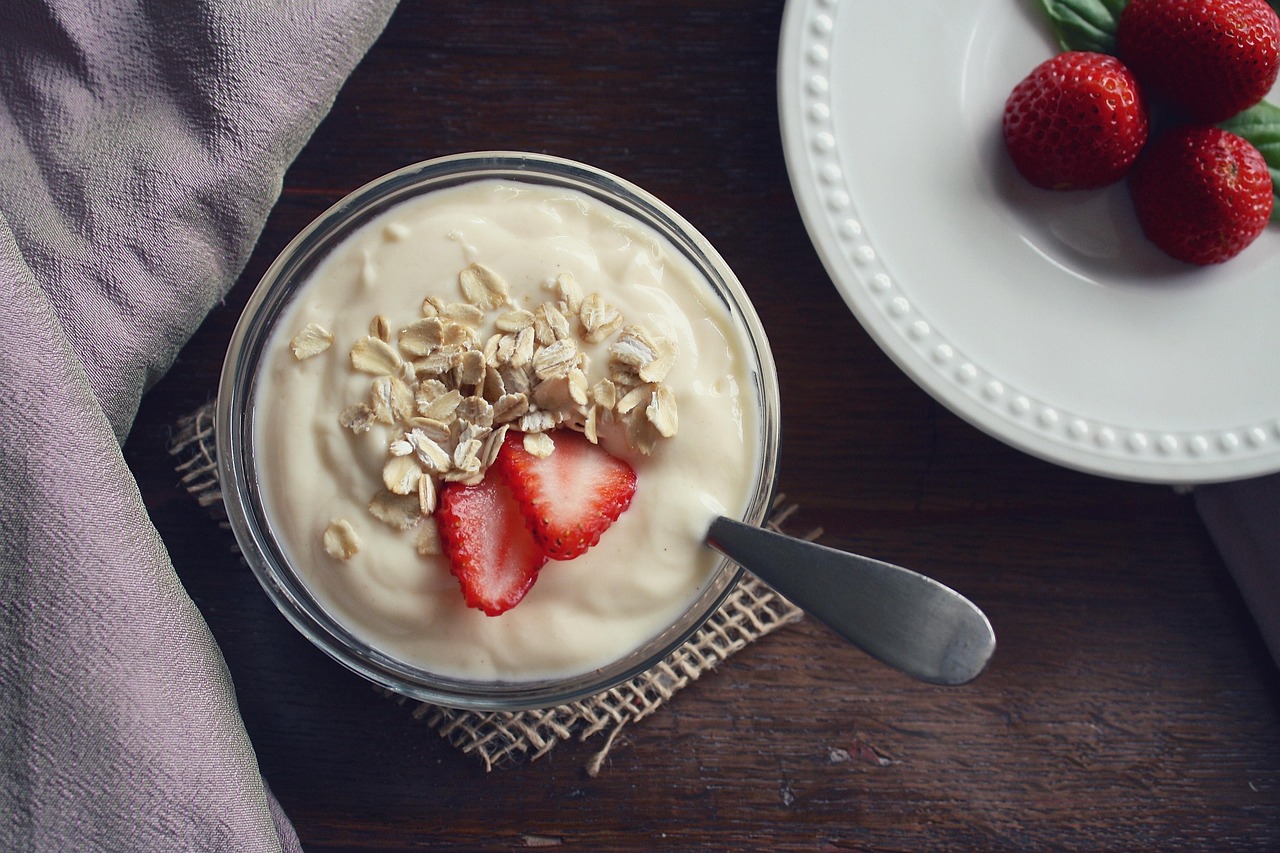 Bowl of Greek yogurt topped with oats and sliced strawberries on a wooden table