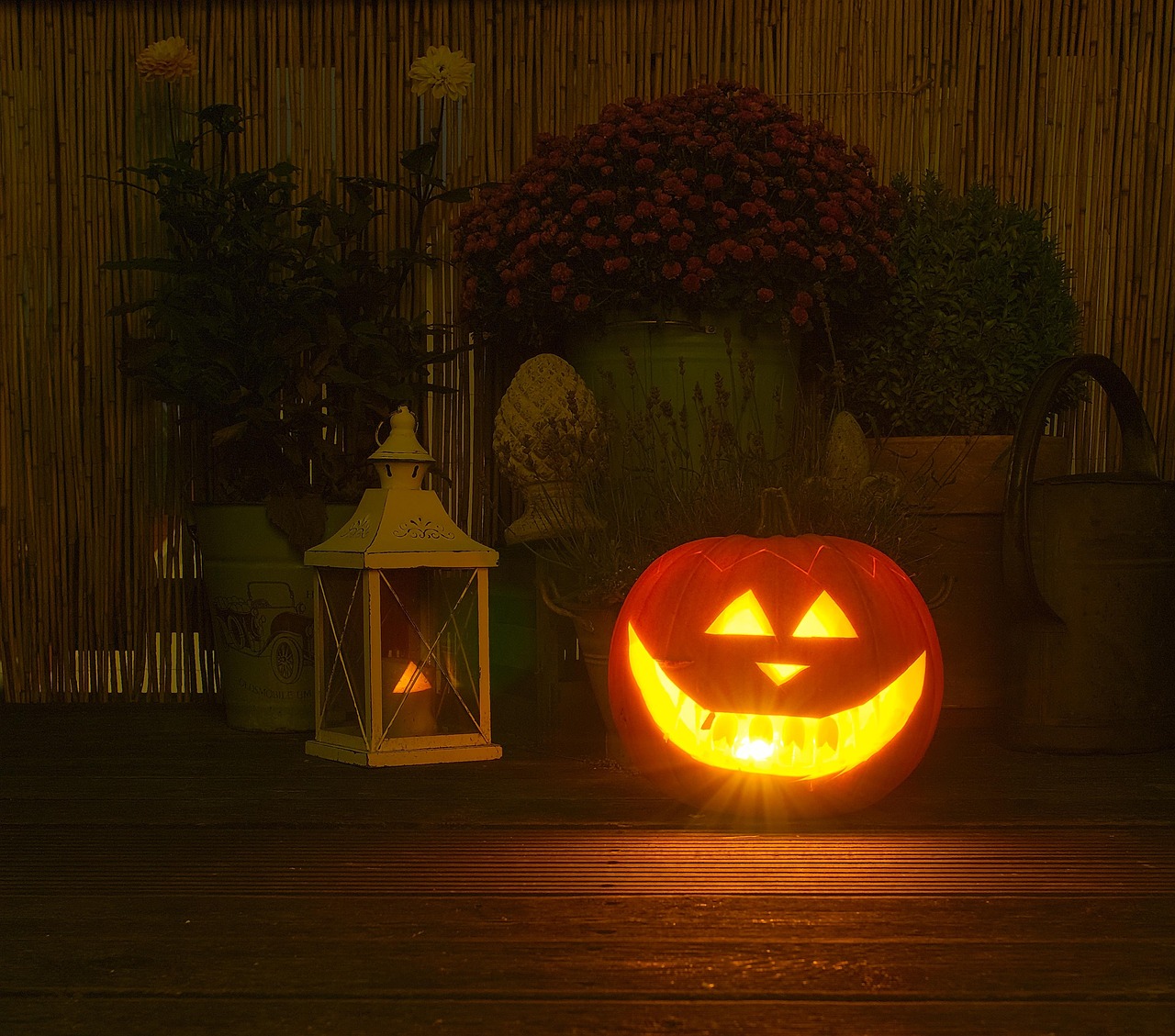 Glowing carved jack-o'-lantern on a front porch at night beside a lantern and potted mums