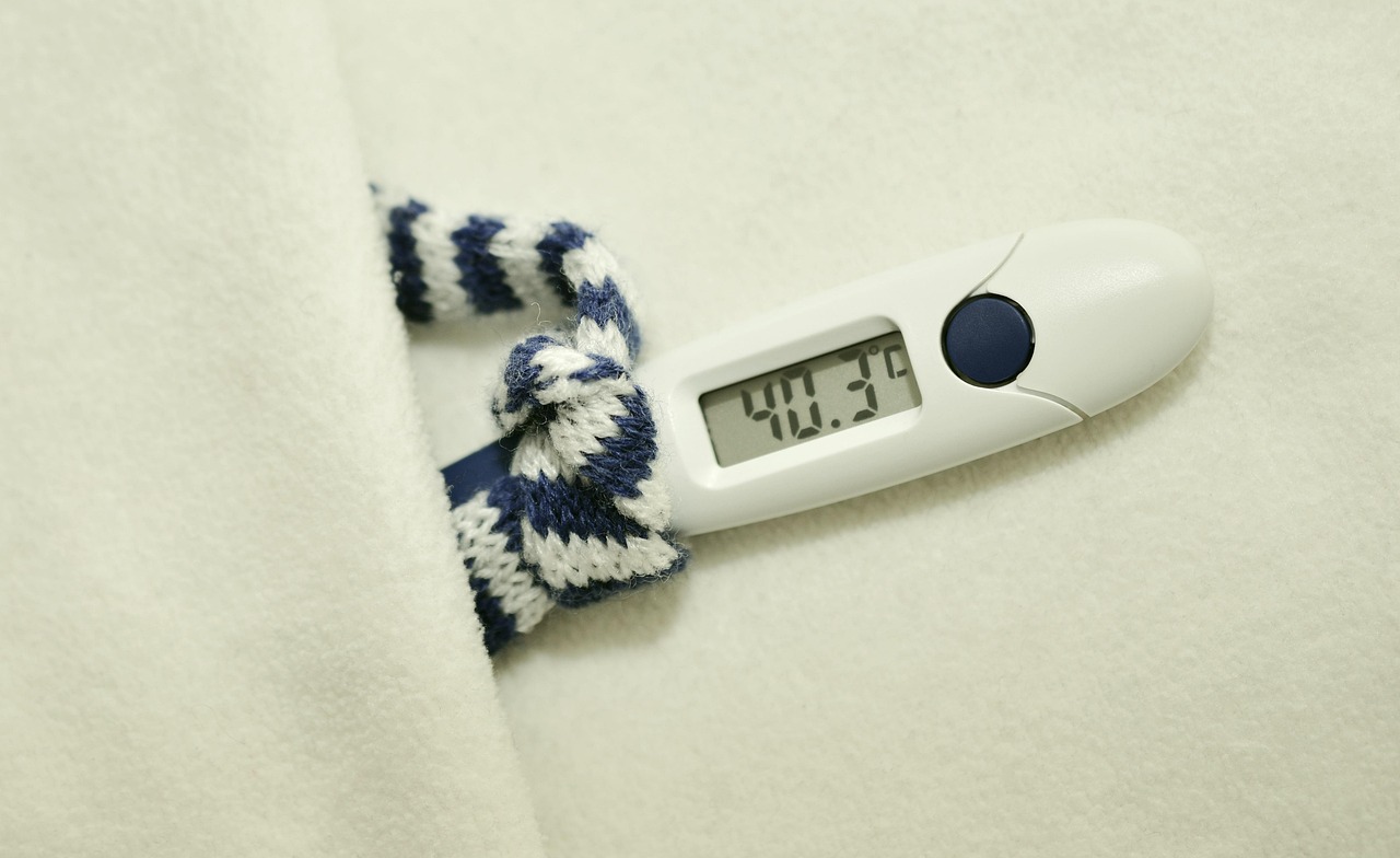 Digital thermometer showing a high fever reading resting on a soft white blanket next to a knit scarf