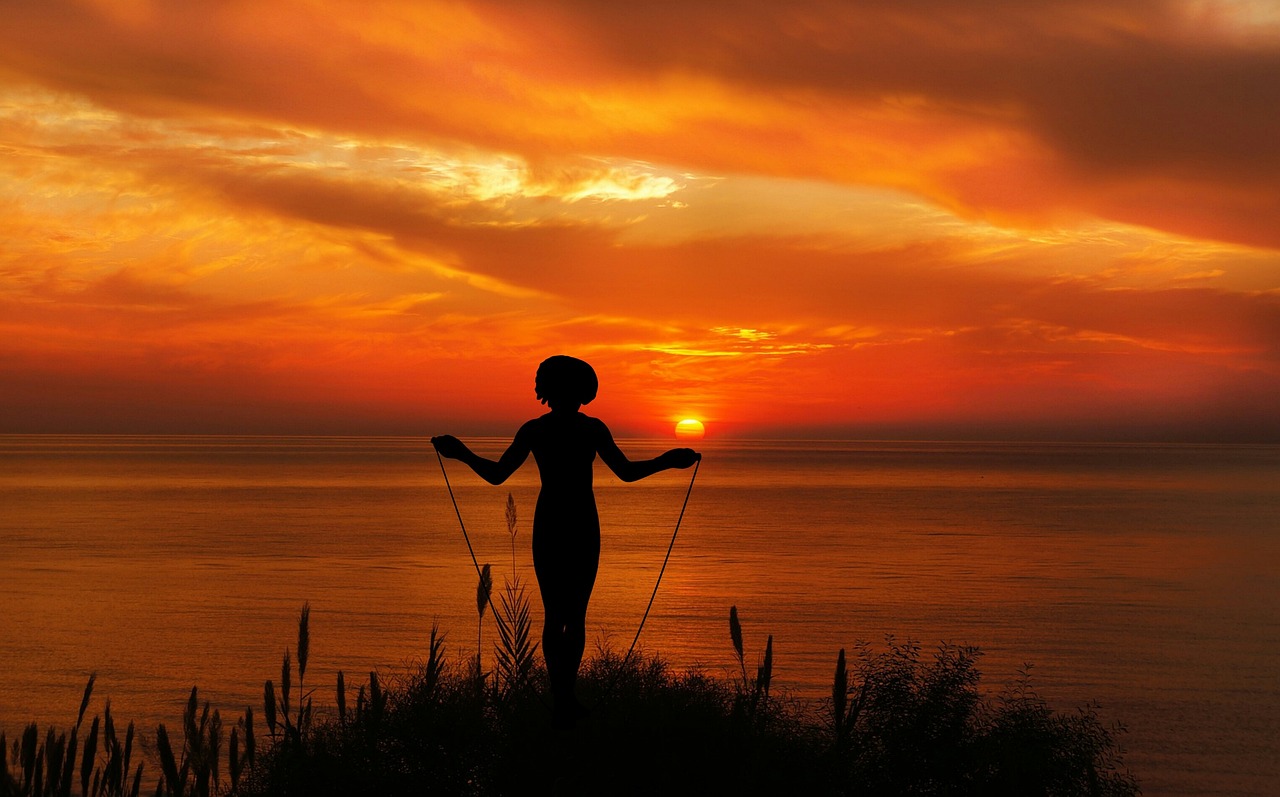 Silhouette of a woman skipping rope at sunset beside the sea