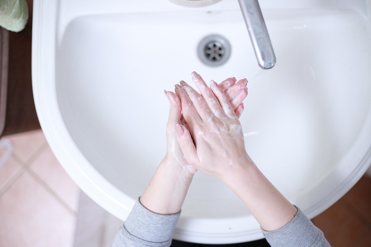 Hands lathered with soap being washed over a white bathroom sink
