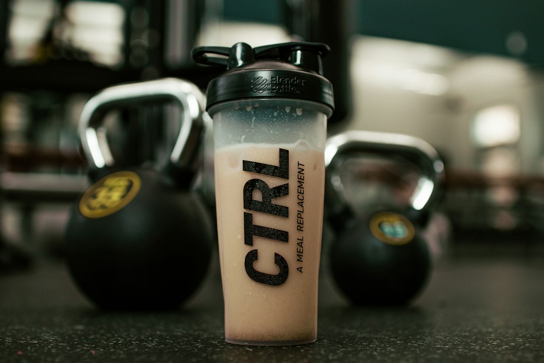 A shaker bottle of a protein drink in a gym beside kettlebells