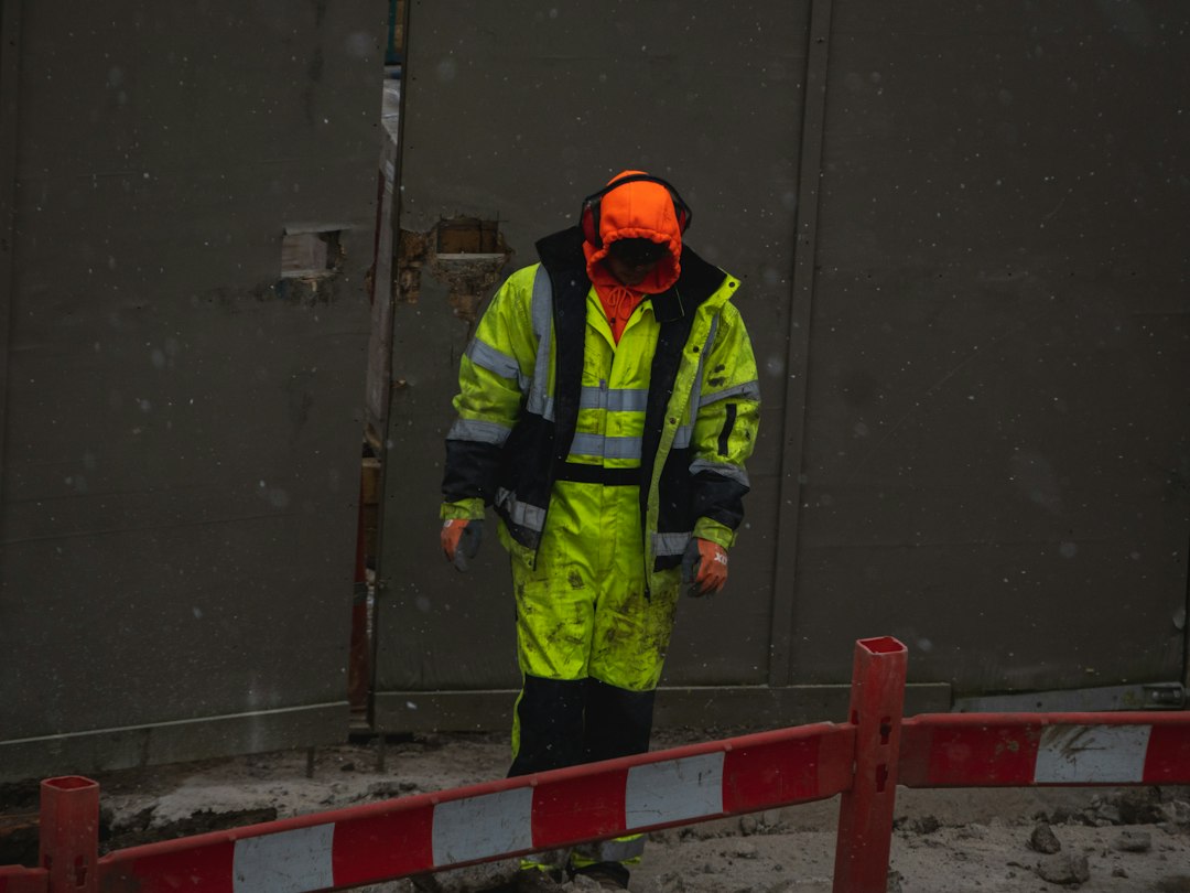 A worker in bright high-visibility clothing with reflective silver stripes standing at a barrier