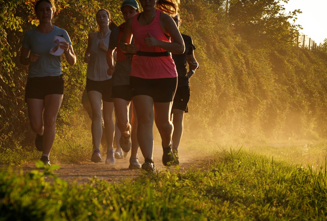 A group of women runners moves along a sunlit trail