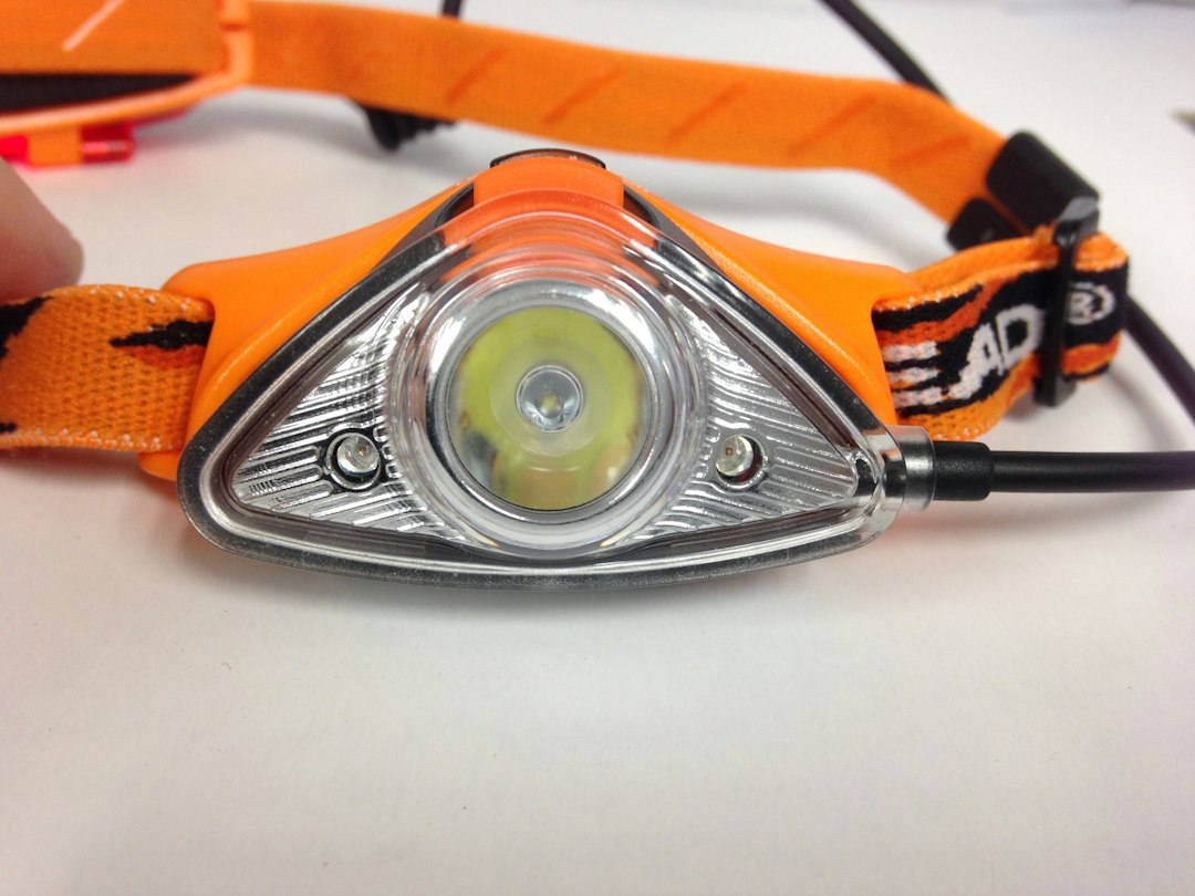A close-up of a bright orange headlamp with a powerful LED beam