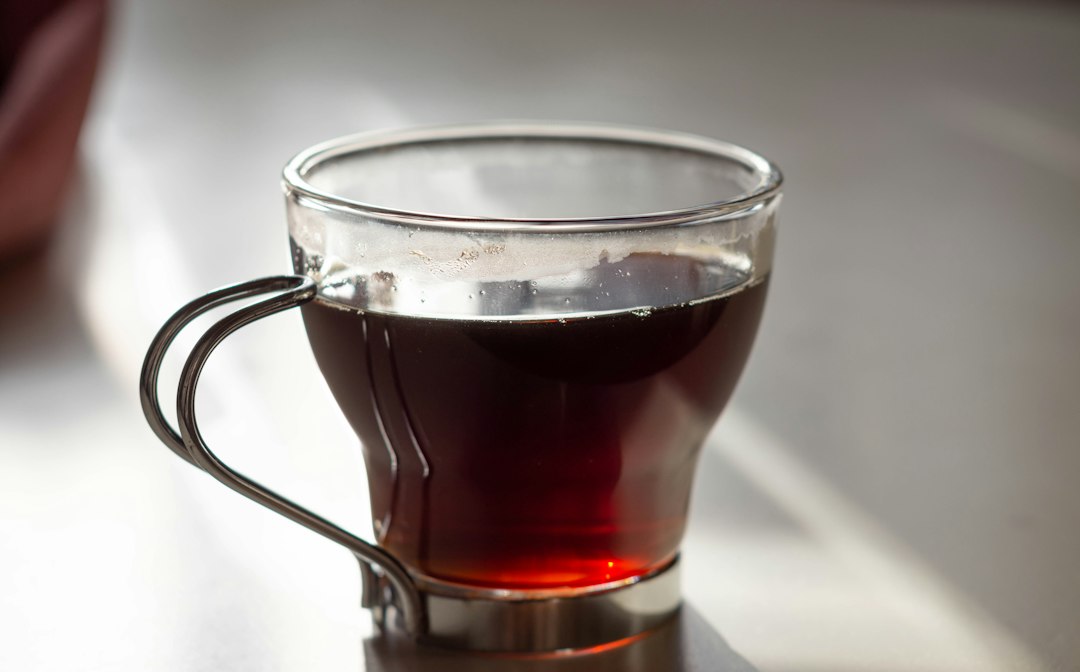 Warm cup of tea in a glass mug with a metal handle catching soft window light