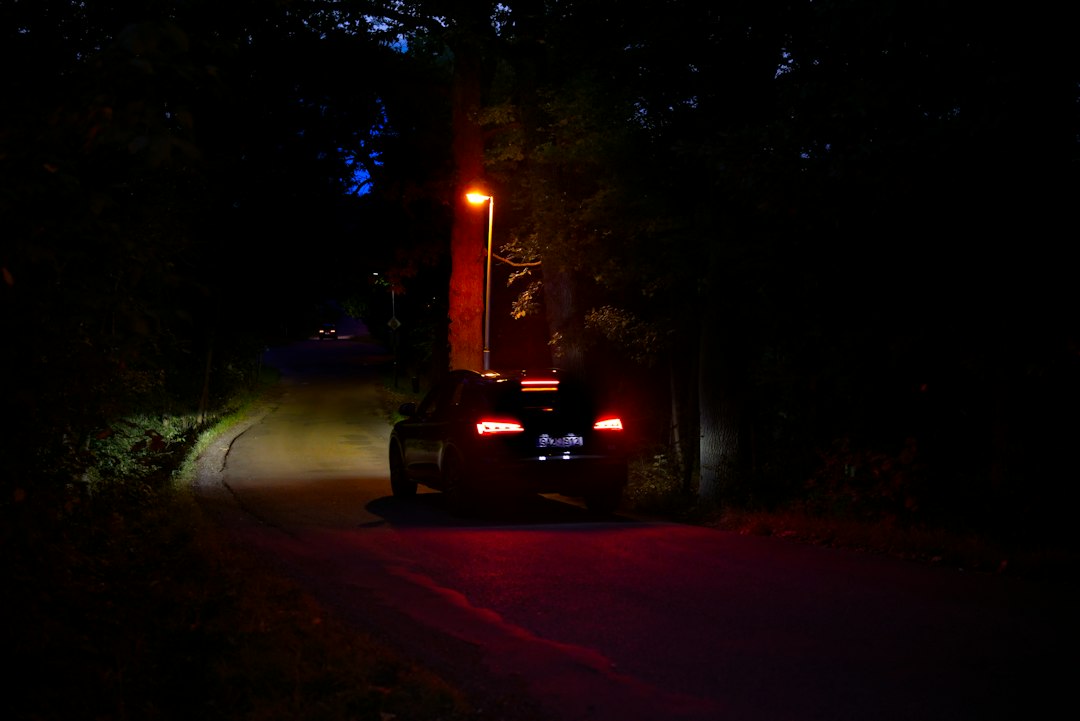 A car with glowing taillights driving down a dark wooded road at night