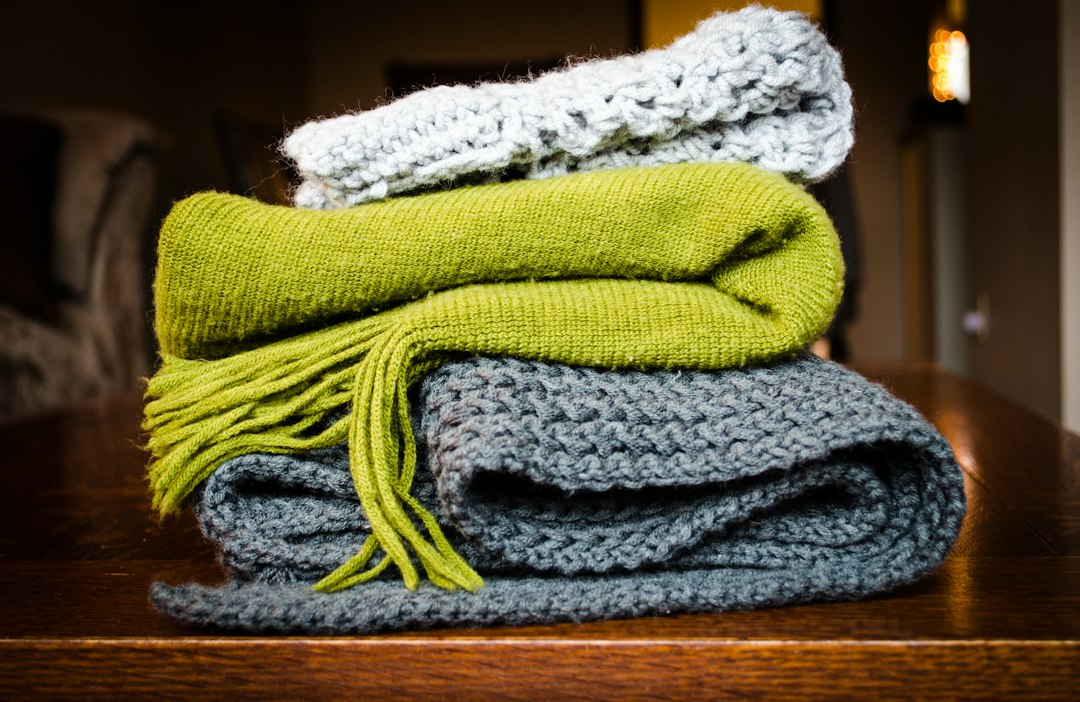 Neatly folded stack of knit blankets in green, blue, and gray