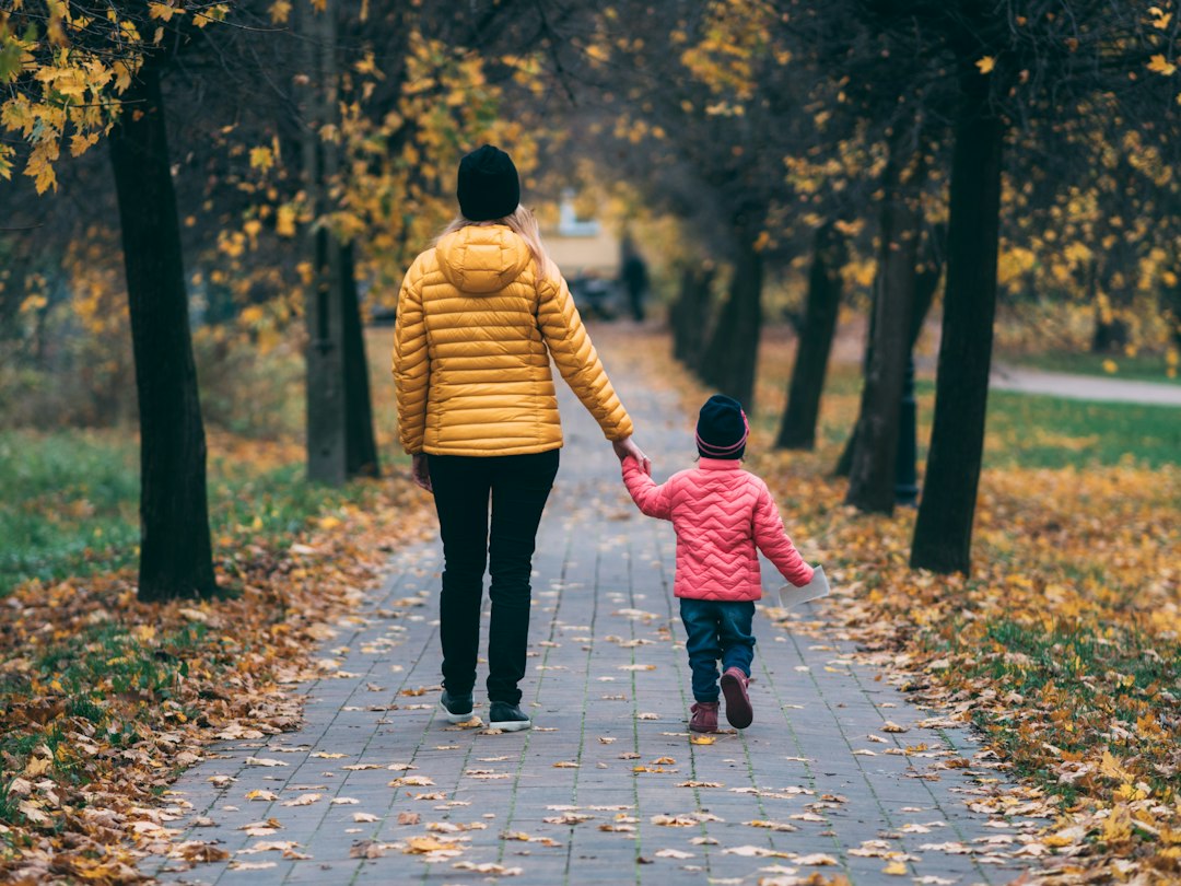 An adult in a yellow puffer jacket walking hand in hand with a child in pink on an autumn path