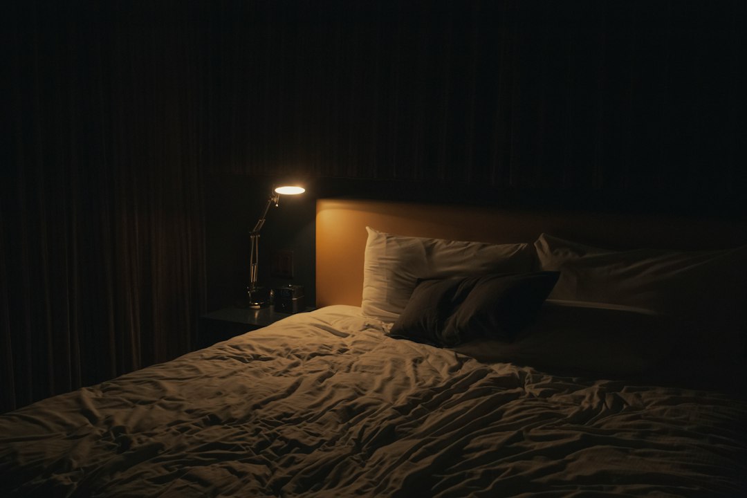 A dark bedroom at night lit only by a small bedside lamp
