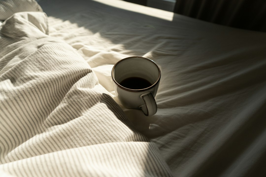 A mug of coffee on rumpled bedsheets in soft morning light
