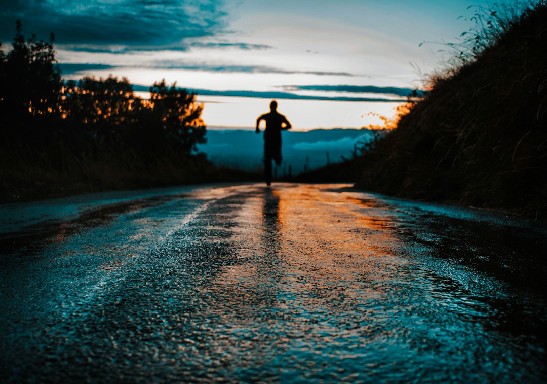 Silhouetted runner training on a wet road in early morning darkness