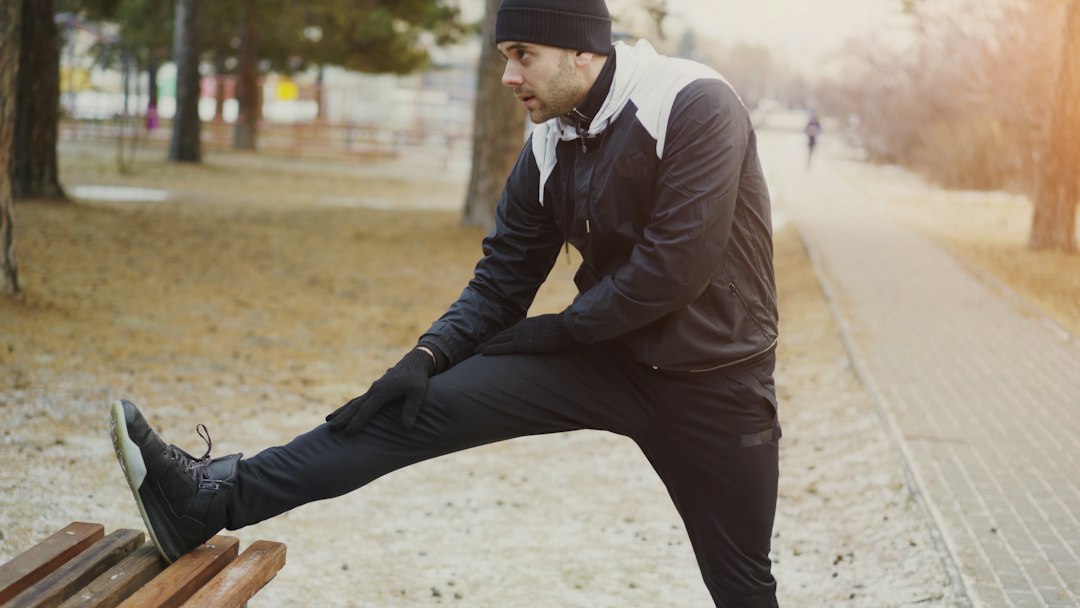 Older man doing a standing leg stretch outdoors on a park path