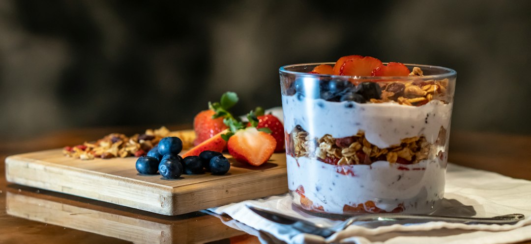 Glass of Greek yogurt layered with granola, blueberries, and sliced strawberries