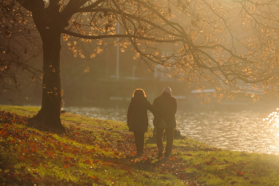 Two people walking together on a leaf-covered path through an autumn park