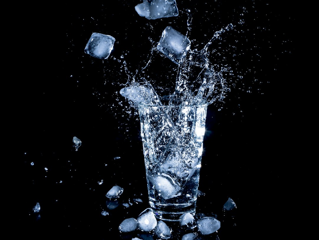 Ice cubes splashing into a tall glass of cold water