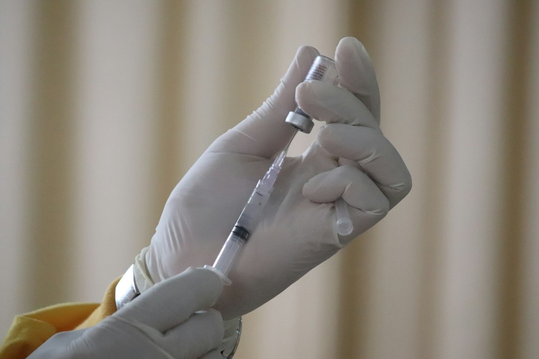 Gloved hands drawing a vaccine dose from a small vial with a syringe