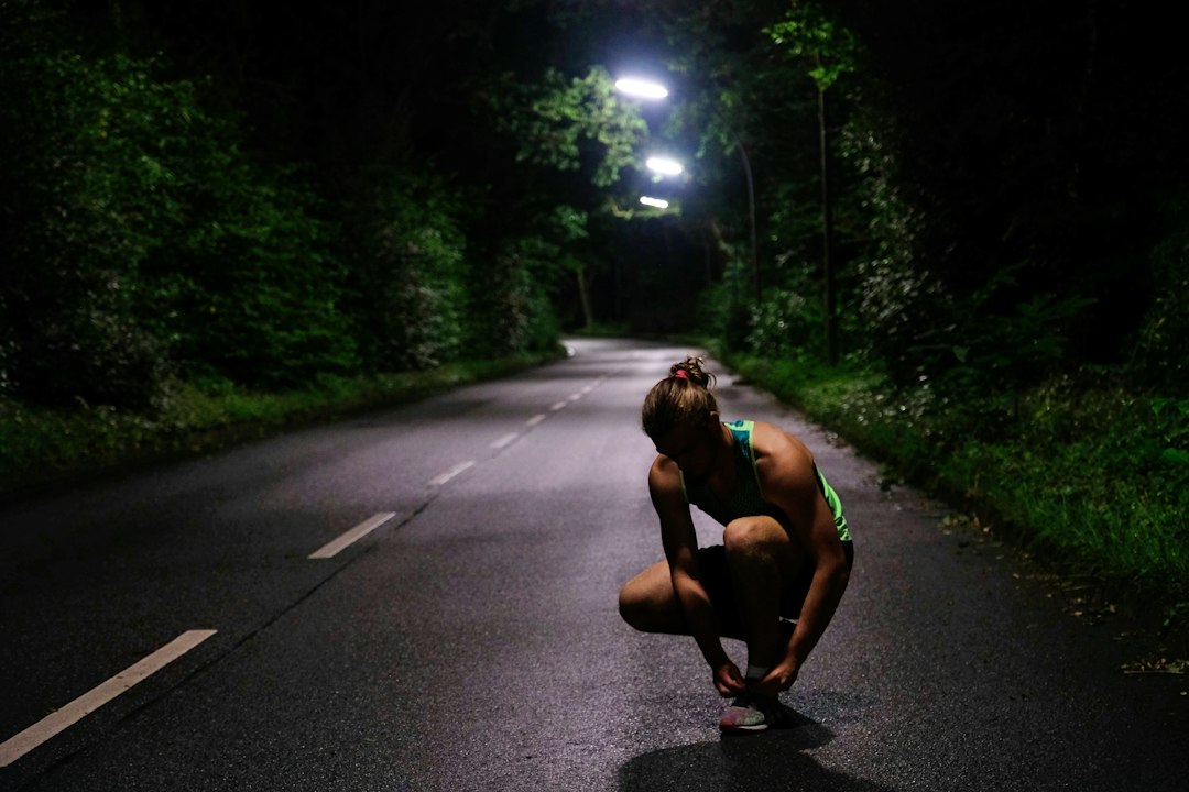 A runner laces up on a road lit by streetlights before sunrise