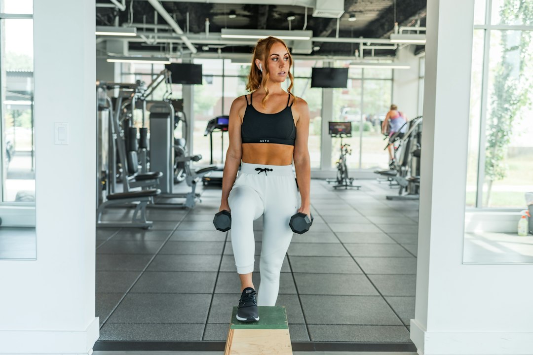 Woman holding dumbbells while performing a weighted step-up onto a wooden box
