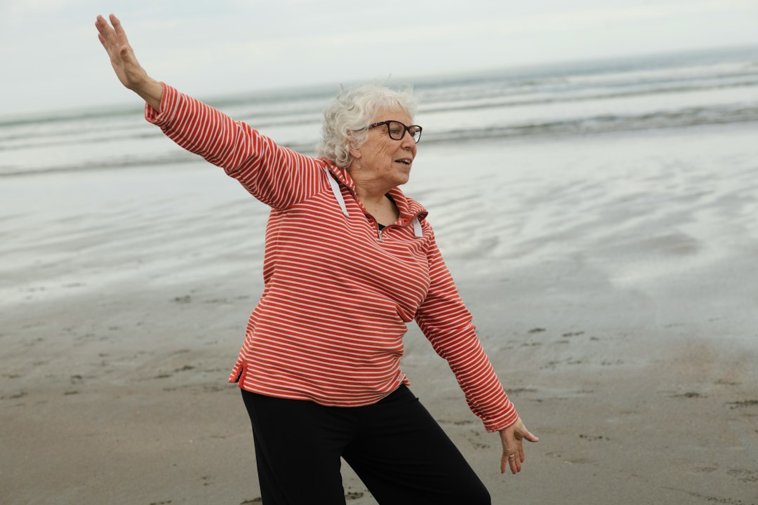 Smiling senior woman standing playfully on a beach with arms raised