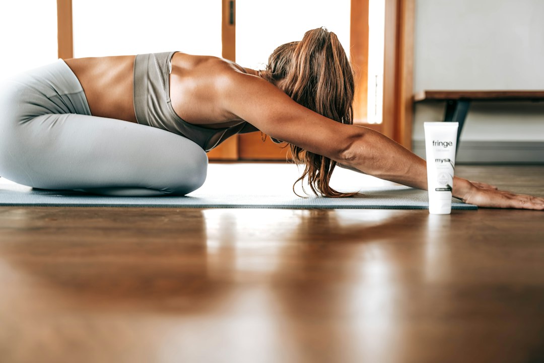 A woman in comfortable clothes stretching on a mat on her living room floor at night