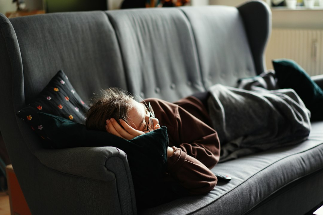 Person resting on a grey couch under a blanket with their head on a pillow
