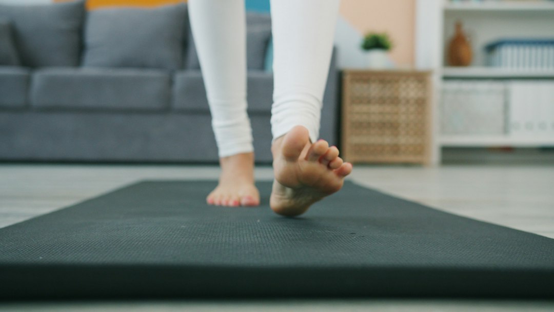 Bare feet stepping slowly onto a dark exercise mat in a bright living room